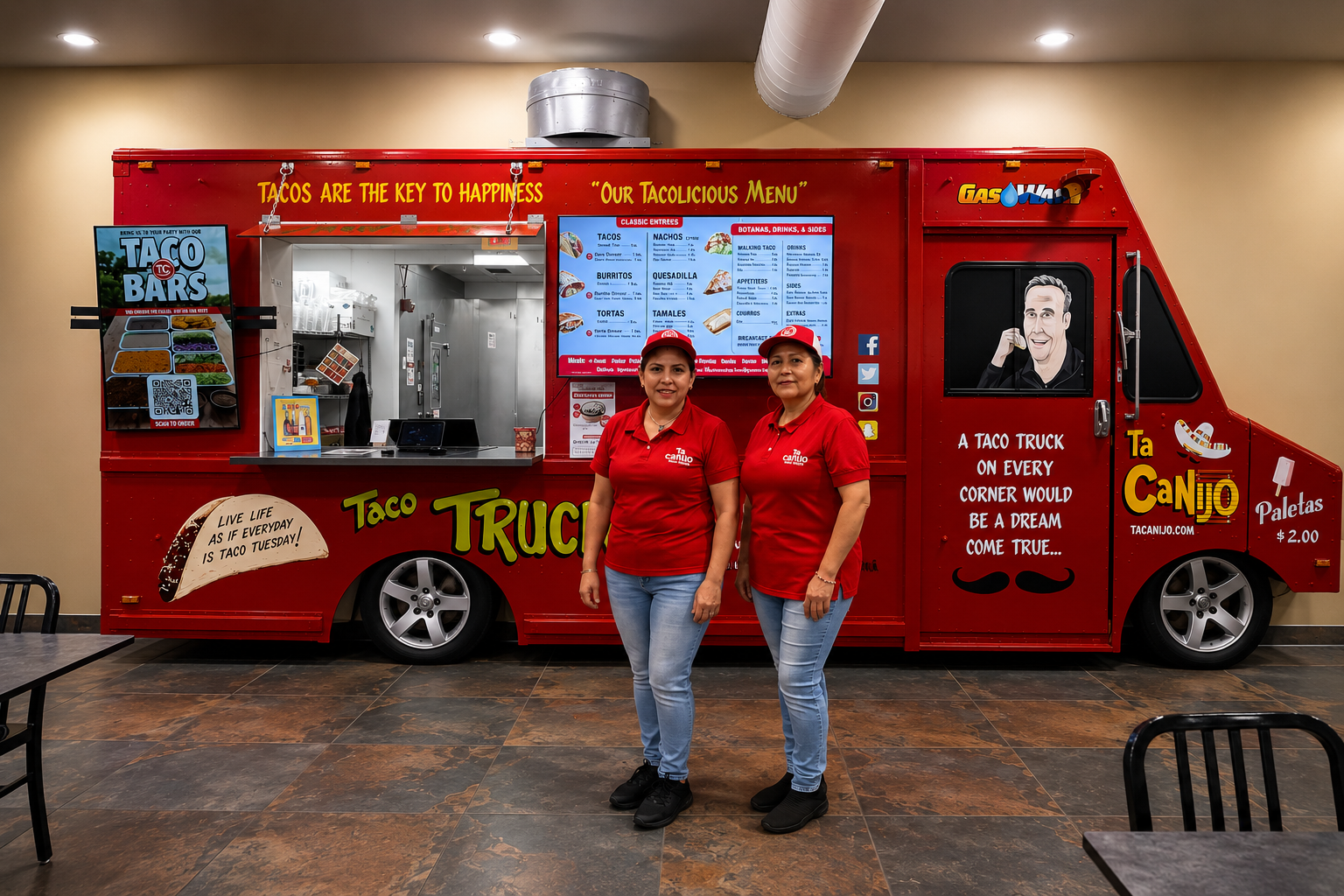 Two smiling Ta Canijo team members in red shirts standing in front of the red taco truck inside the restaurant